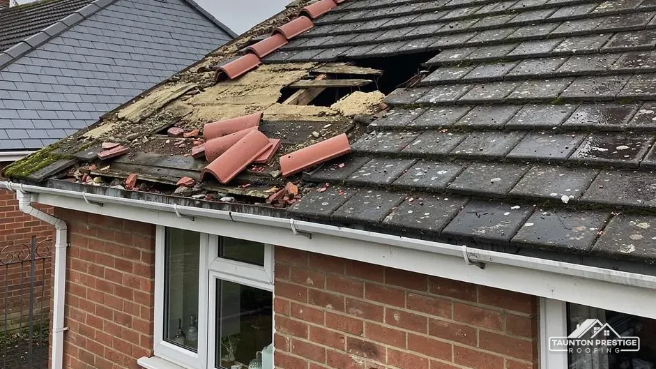 Storm-damaged bungalow roof with a hole, broken ridge tiles and loose debris