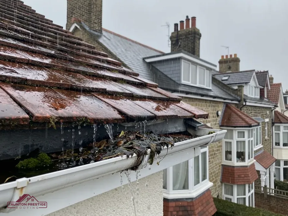 Blocked gutter overflowing with rainwater below a tiled roof