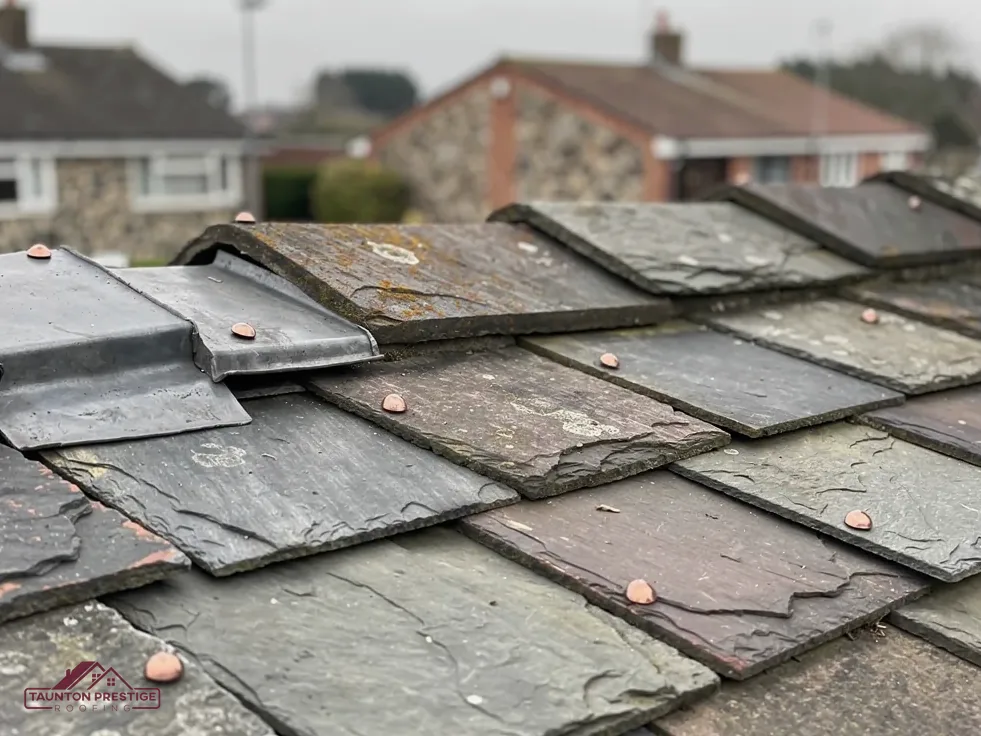 Close-up of weathered natural slates held with copper nails beside a lead flashing