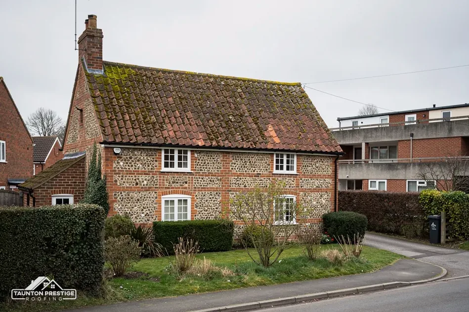 Flint and brick cottage with a mossy clay tile roof on a street corner