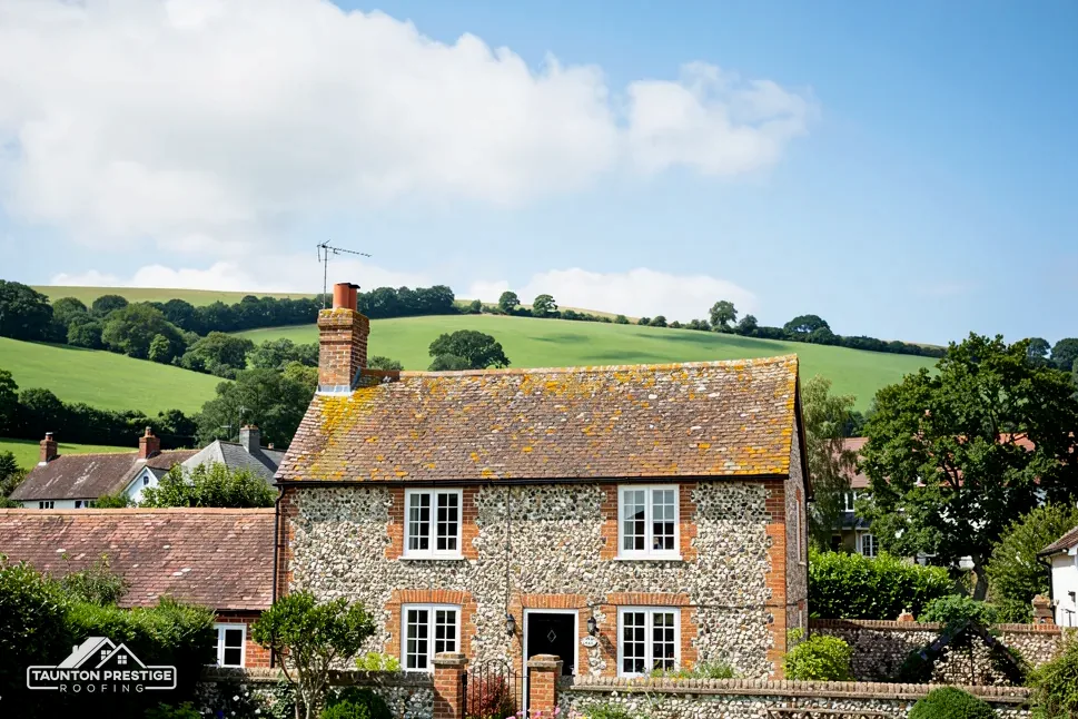 Flint and brick cottage with a clay tile roof among gardens and green hills